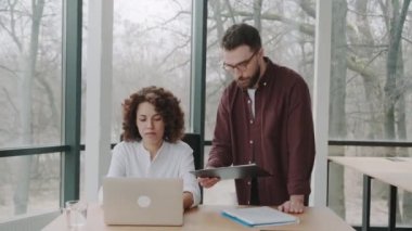 İki çok ırklı çalışan dizüstü bilgisayarın yakınındaki bir projeyi tartışıyorlar. Afrika kökenli Amerikalı kadın ve Avrupalı erkek birlikte çalışarak ortak çalışma alanındaki mali raporları analiz ediyorlar..