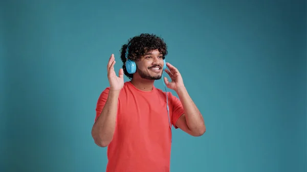 若い笑顔の幸せなラテン語やアラビア語の男性20代のヘッドフォンで音楽を聴くと 青いスタジオの背景で楽しいです 人々のライフスタイルコンセプト — ストック写真