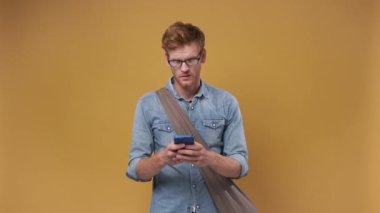 Genç kızıl saçlı yakışıklı adam şaşkınlıkla akıllı telefona bakıyor, kötü internet servisinden memnun değil. kahverengi stüdyo arka planı