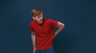 İzole edilmiş mavi arka planda çabaladığı için sırt ağrısı çeken beyaz, yakışıklı bir adam.