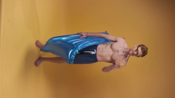 垂直录像 红头发男子在海滩短裤与充气床垫和鸡尾酒 黄色背景的暑假概念 — 图库视频影像