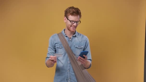 Young Bearded Man Holds Credit Card Smartphone Isolated Orange Background — Stock Video