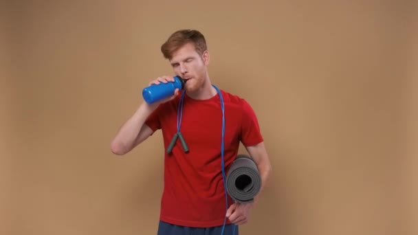 Schöner Mann Mit Yogamatte Trinkt Wasser Auf Beigem Hintergrund — Stockvideo