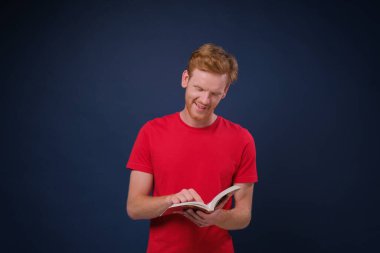 Kitap okuyan ve gülümseyen genç bir adamın resmi mavi arka planda izole edilmiş.