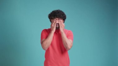 Genç, yakışıklı, esmer adam gözlerini ovuşturuyor. Gözlerinde yorgunluk ve acı hissediyor. Mavi bir stüdyonun arka planında duruyor.