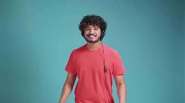 Genç Latin ya da Arap çağrı merkezi ajanı mercan tişörtlü mavi stüdyo arkasında kulaklık takıyor ve gülümseyen bir yüzle baş parmağıyla işaret ediyor..