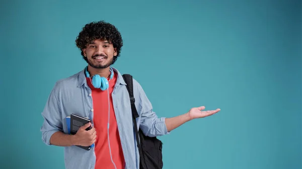 若い学生インド人またはスペイン人男性バックパック付きブルースタジオの背景にあなたの製品を提示側を指している — ストック写真