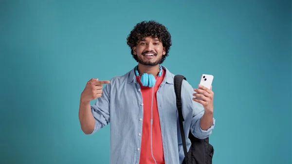 幸せな若いラテン系スペイン人男性お勧め素晴らしいポッドキャストやオンライン音楽プラットフォーム 購読を購入するいつでも曲を聞く ヘッドフォンを着用 電話でポイント — ストック写真