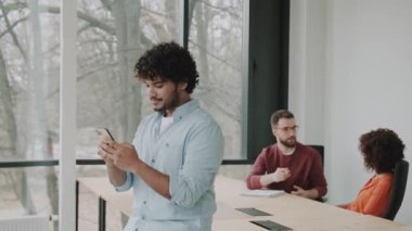 Mutlu genç Latin iş adamı yöneticisi, iş adamı yönetici, ofisinde oturmuş akıllı telefon kullanıyor cep telefonu kullanıyor iş yerinde dijital teknoloji işlemlerini yönetiyor..