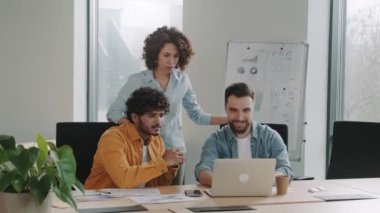 Ofisteki çok ırklı çalışanlar dizüstü bilgisayara bakıp şirket başarısını kutluyor. Ortaklık kazanılıyor.