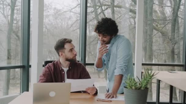 Двоє Міжнародних Співробітників Сучасному Офісі Дружньо Спілкуються Біля Ноутбука Посміхаються — стокове відео