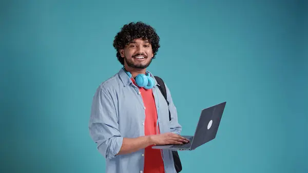 陽気なハンサムな多民族の学生は青いスタジオの背景にネットブックのノートパソコンと笑顔を持っています ストック画像