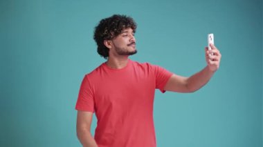 Latin kökenli Latin bir adam mavi stüdyo arka planında selfie çekerken profilde görünüyor.