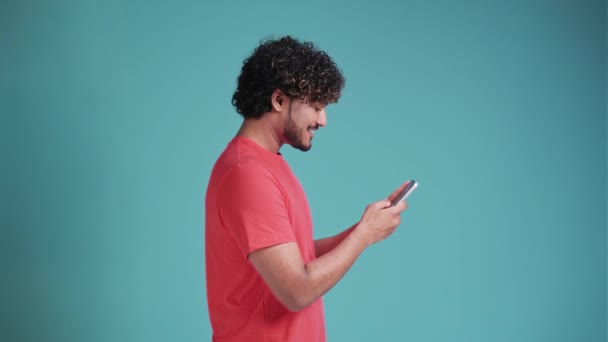 fun young bearded multi-ethnic man 20s years old hold in hand use mobile cell phone typing browsing chatting send sms in coral t-shirt on blue studio background studio