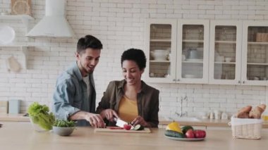 Genç çift sağlıklı yemek pişirirken ve salata hazırlarken eğleniyor. Sağlıklı beslenme ve vejetaryenlik kavramı.