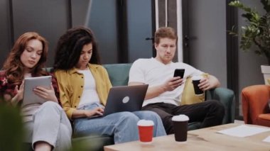 Üç genç çok ırklı insan farklı araçlar kullanıyor veya kullanıyor, akıllı telefon, dizüstü bilgisayar ve tabletle.