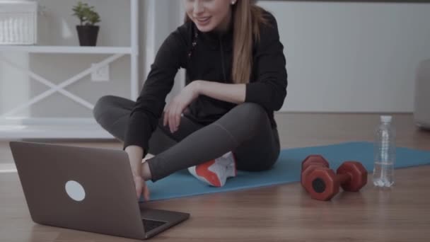 自宅でスポーツトレーニングでトレーニングビデオを見ている女の子 ダンベル近くのマットに座って — ストック動画