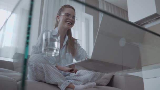 ハッピー笑顔の女性はソファーに座って 自宅でラップトップを使用して 画面を見て笑って 面白いビデオを見ています — ストック動画