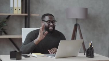 Siyah adam elini bir dizüstü bilgisayara daldırıyor ve ofisteki günlük kıyafetlerle video bağlantısıyla iletişim kuruyor.