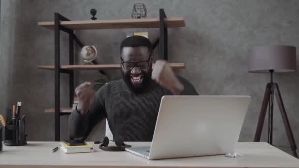 快乐的非洲千禧一代坐在桌旁看着笔记本电脑屏幕感到兴奋收到好消息在线彩票中奖者欢欣鼓舞在家里 男子得到提升或奖励 雇用的梦想工作概念 — 图库视频影像