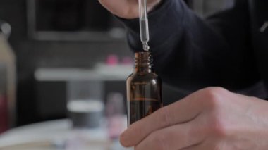 Bir adamın ellerinin içinde kozmetik sıvı bulunan bir şişeyi pipetle tutarken yakın plan fotoğrafı.