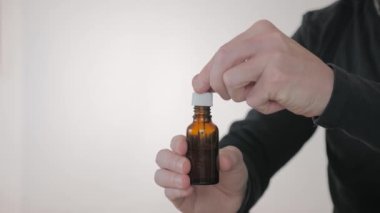 Bir adamın ellerinin içinde kozmetik sıvı bulunan bir şişeyi pipetle tutarken yakın plan fotoğrafı.