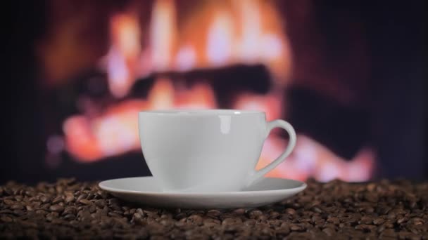 コーヒー豆に立っているコーヒーカップ バックグラウンドで暖炉を燃やす — ストック動画