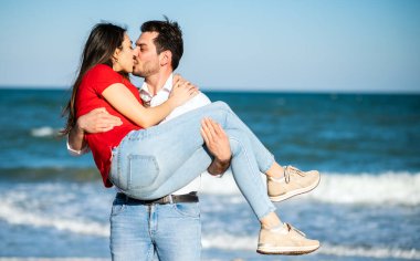 Romantik bir adam sahilde kız arkadaşını kollarında tutuyor.