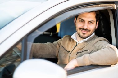 Genç adam yeni arabasında güvenle gülümsüyor.