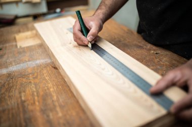 Marangoz tezgahın üzerinde tahta bir kalas ölçüyor.