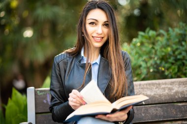 Parktaki bankta kitap okuyan güzel bir üniversite öğrencisi.