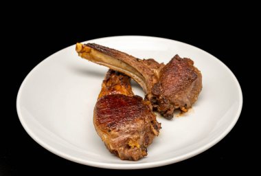 Beyaz tabakta ızgara kuzu pirzolası, siyah arka planda izole edilmiş..