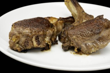 Beyaz tabakta ızgara kuzu pirzolası, siyah arka planda izole. Yakın çekim görünümü.