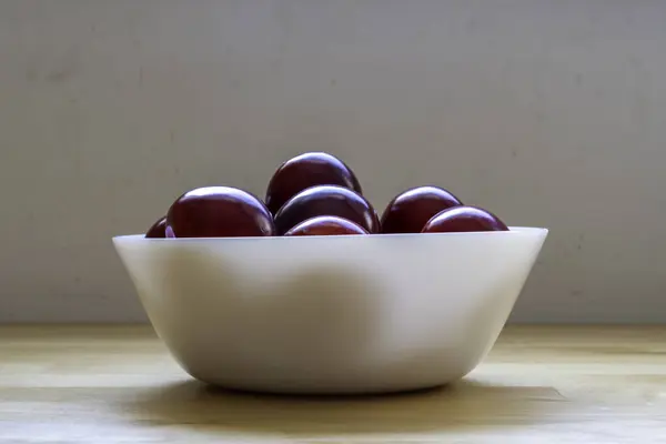 Red sour plums in a white ceramic bowl. Side view.