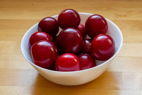 Red sour plums in a white ceramic bowl.