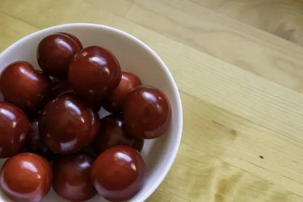 Red sour plums in a white ceramic bowl. High angle view.