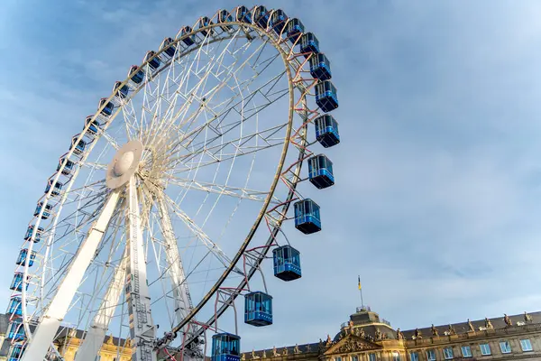 Berrak mavi gökyüzünün altında Avrupa tarzı tarihi bir binanın üzerinde mavi yolcu kuleleri olan canlı bir dönme dolap..