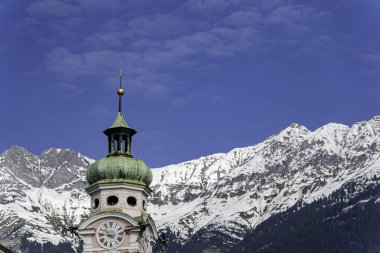 Yeşil bakır kubbeli tarihi saat kulesi karla kaplı Alp dağları ve parlak mavi gökyüzü karşısında Avrupa dağ kasabalarının cazibesini yakalıyor..