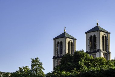 Yeşil çatıları ve altın haçları olan ikiz kilise kuleleri Salzburg, Avusturya 'da açık mavi bir gökyüzünün altında yemyeşil ağaçların üzerinde yükseliyor..