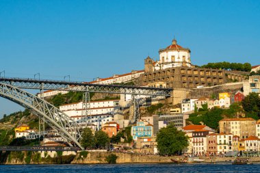 Tarihsel Serra do Pilar Manastırı ve Portekiz 'in Vila Nova de Gaia kentindeki sembolik Dom Luis Köprüsü, renkli nehir kenarlı binalar ve açık mavi gökyüzü ile Douro Nehri' nden izleniyor..