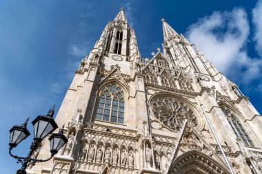 Viyana, Avusturya 'da göz kamaştırıcı bir neo-gotik katedrali olan Votivkirche' in alçak açılı manzarası, karmaşık mimarisi ve parlak mavi gökyüzünün altında ikiz kuleleri var..