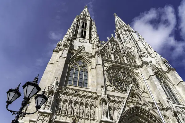 Viyana, Avusturya 'da göz kamaştırıcı bir neo-gotik katedrali olan Votivkirche' in alçak açılı manzarası, karmaşık mimarisi ve parlak mavi gökyüzünün altında ikiz kuleleri var..
