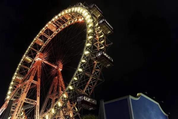 Geceleyin, bir lunaparktaki karanlık gökyüzüne karşı parlak kırmızı ve sarı ışıklarla aydınlanan dev dönme dolap..