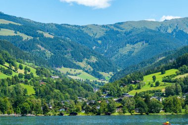 Mountain village with green hillsides and lakefront under clear summer skies.