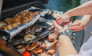 Barbekü pişirmek. Beyaz tişörtlü bir adam ızgarada barbekü yapıyor..
