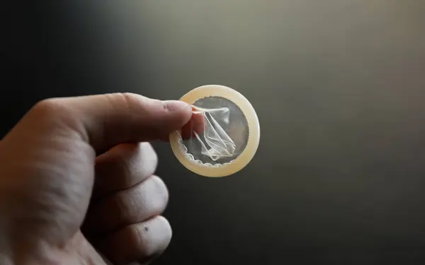 Siyah arka planda prezervatifli bir el. Doğum kontrol kavramı