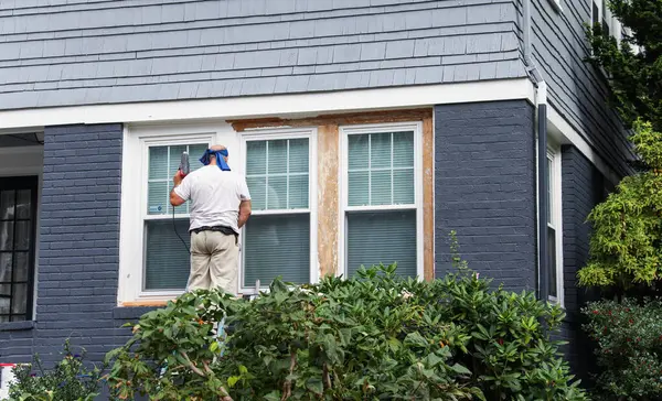 Koruyucu üniformalı bir adam pencereyi silindirle boyuyor.