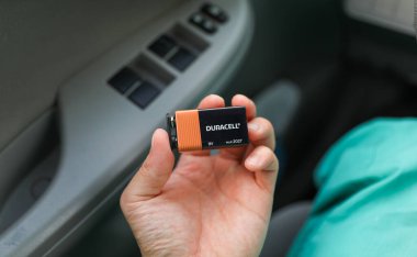 Kadının biri elinde araba aküsü tutuyor.