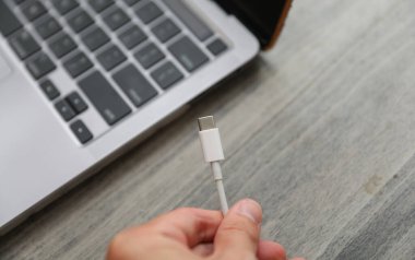 Adam elinde dizüstü bilgisayarla USB kablosu tutuyor..