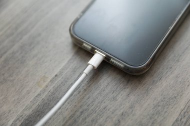 Akıllı telefon beyaz ahşap bir masada şarj oluyor.